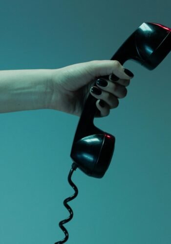 Moody close-up of a hand holding a vintage telephone receiver against a blue background.
